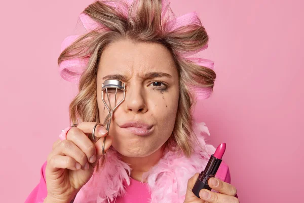 Foto colorida com fundo rosa que mostra uma mulher com maquiagem borrada - Metrópoles.