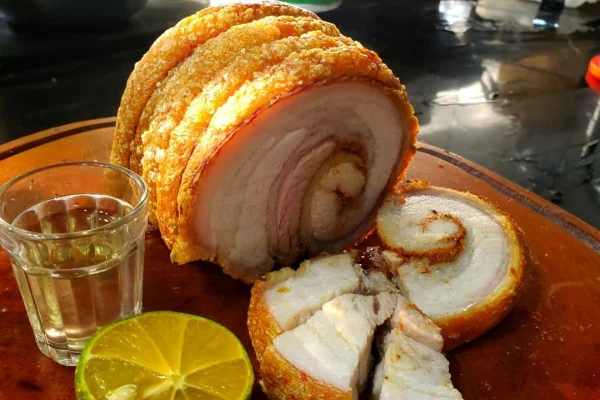 torresmo de rolo servido em bandeja de madeira ao lado de um copo de cachaça e limão