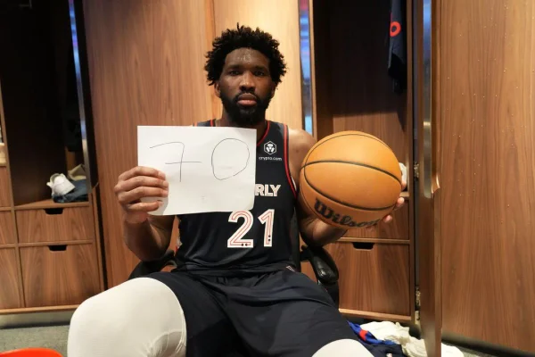 Jogador do 76ers Joel Embiid segurando cartaz com o numero 70 e uma bola de basquete