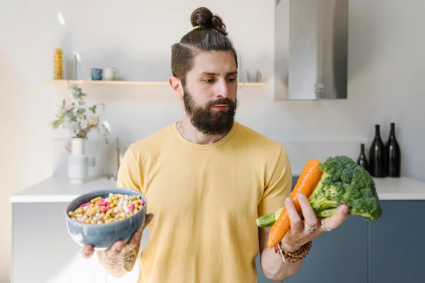 Foto colorida de homem branco e com barba grande. Ele segura uma tigela de comprimidos e vegetais - Metrópoles