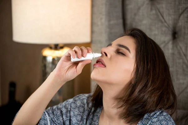 Imagem colorida de mulher com a cabeça inclinada para usar descongestionante nasal - Metrópoles