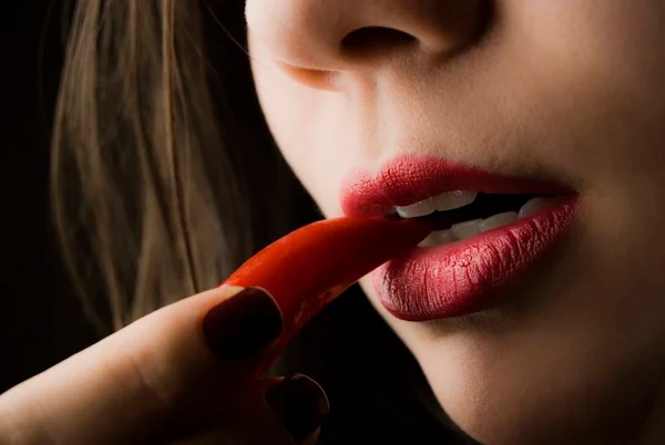 Mulher de batom vermelho com uma pimenta na boca