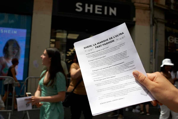 Uma jovem segura um folheto contra a SHEIN, explicando por que o fast fashion é um problema para o meio ambiente.