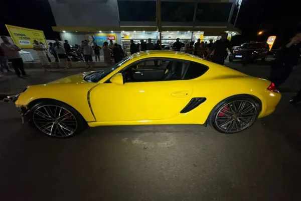 Porsche amarela centralizada na imagem, com um comércio ao fundo.
