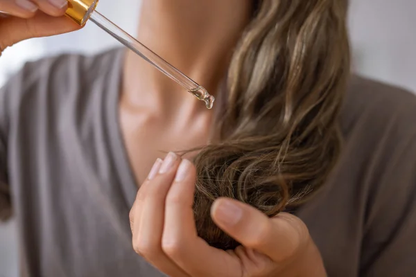 Foto colorida de mulher aplicando óleo no cabelo - Metrópoles