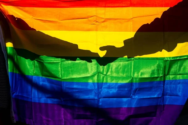 Silhueta de mãos dadas atrás de bandeira LGBTQIA+