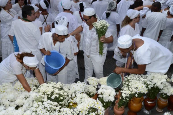 Foto colorida de pessoas vestidas de branco com flores brancas, celebrando religião de matriz africana - Metrópoles