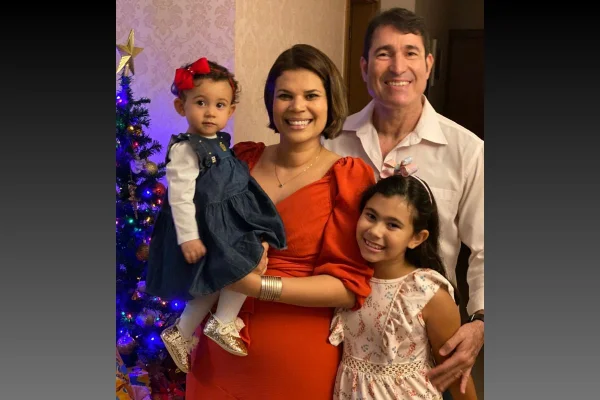 Imagem colorida: família com mãe, pai e duas filhas crianças em frente a árvore de Natal - Metrópoles