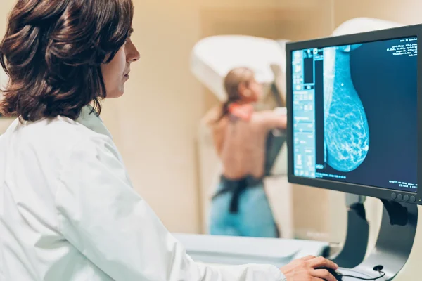 Foto de mulher fazendo mamografia ao fundo e médica analisando exame - Metrópoles