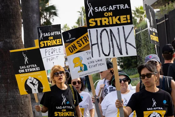 Foto colorida da greve dos atores de Hollywood. Pessoas seguram placas - Metrópoles