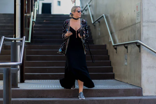 Mulher branca com vestido longo descendo as escadas. Ela usa óculos escuros, cabelo preso e está segundo uma bolsa de mão - Metrópoles