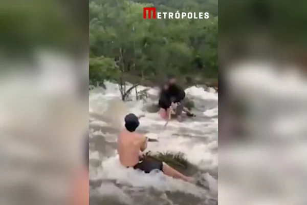 Imagem colorida de pessoas se segurando para não serem arrastadas por enxurrada - Metrópoles