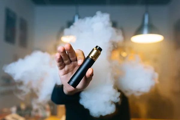 Imagem colorida de homem segurando cigarro eletrônico com muita fumaça ao fundo