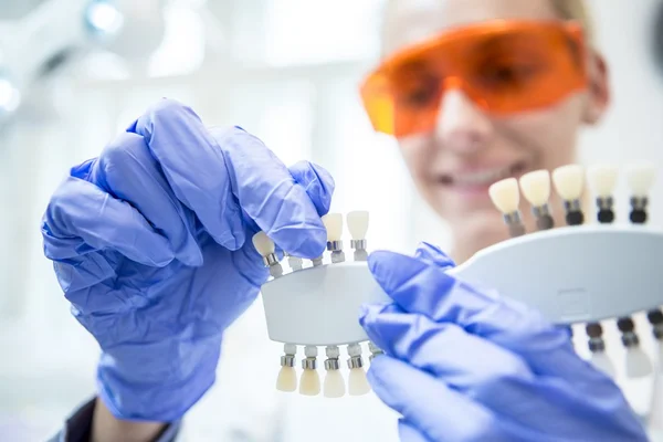 Imagem colorida mostra mulher dentista de óculos laranja escolhendo a tonalidade de lente de contato dentária - Metrópoles