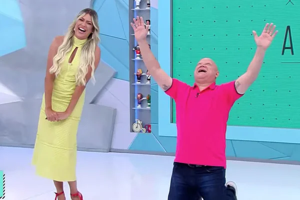 Renata Fan, de vestido amarela, ri da comemoração de Ronaldo Giovaneli, ajoelhado com as mãos para o céu, no Jogo Aberto - Metrópoles