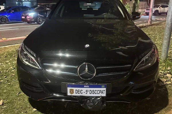 Imagem colorida mostra frente de Mercedes Benz C180 preta com placa coberta - Metrópoles