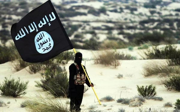 Imagem colorida mostra membro do Estado Islâmico segurando a bandeira do grupo terrorista - Metrópoles