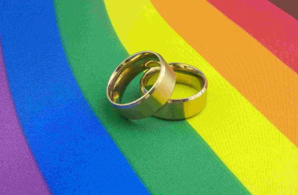 Na foto, alianças de casamento sobre bandeira LGBT+