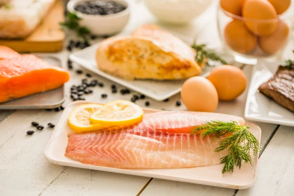 Peixe tilápia cru no prato, frango e ovos no fundo - Metrópoles