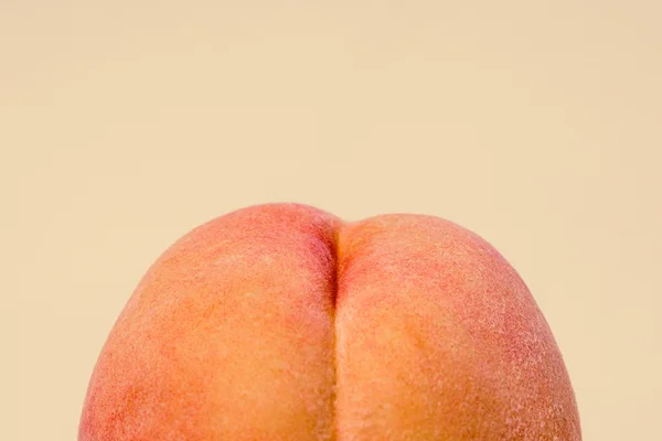 Foto colorida de um pêssego em um fundo laranja claro - Metrópoles