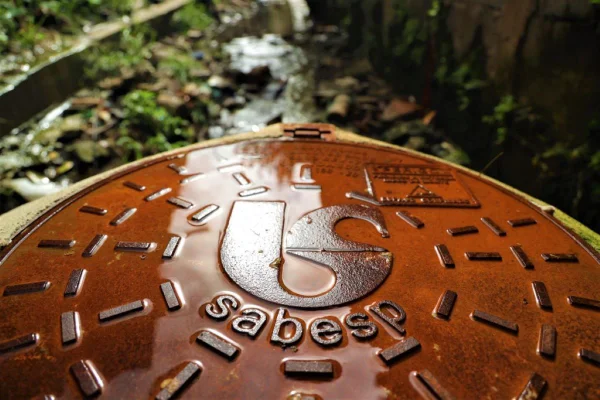 Fotografia colorida mostra bueiro com o logo da Sabesp, a Companhia de Saneamento Básico do Estado de São Paulo