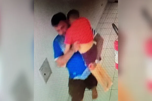 Imagem colorida de homem com enteado no colo inconsciente. Metrópoles
