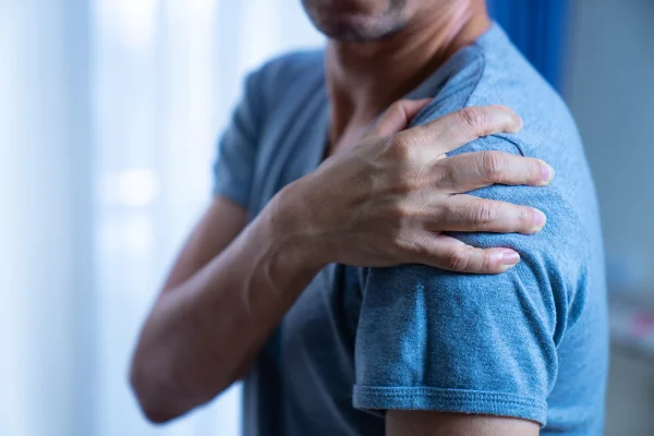 Imagem mostra homem de camiseta azul segurando o ombro - Metrópoles