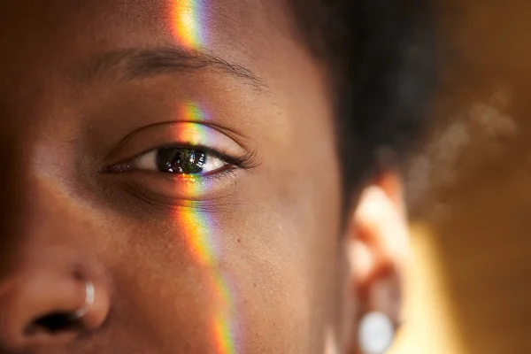 Foto colorida. Imagem foca no olho da mulher negra e um fecho de luz do sol está focado técnico em óptica