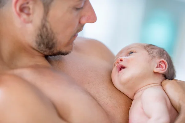 Um pai embala seu bebê recém-nascido contra seu peito nu. Metrópoles