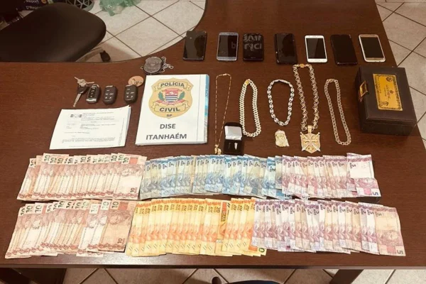 Imagem colorida de dinheiro e joias apreendidos pela polícia. Material está sobre uma mesa - Metrópoles