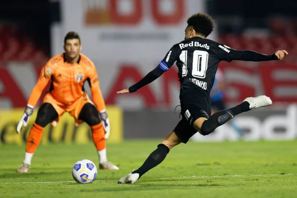 Jogador chuta a bola enquanto goleiro espera para tentar defender