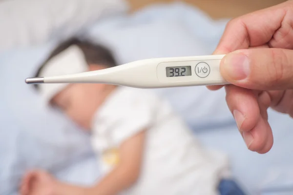 Febre, termômetro médico em close-up, pai medindo a temperatura de seu filho doente, menino asiático de 3 a 4 anos com febre alta deitado na cama com compressa fria na testa para baixar a febre. Metrópoles