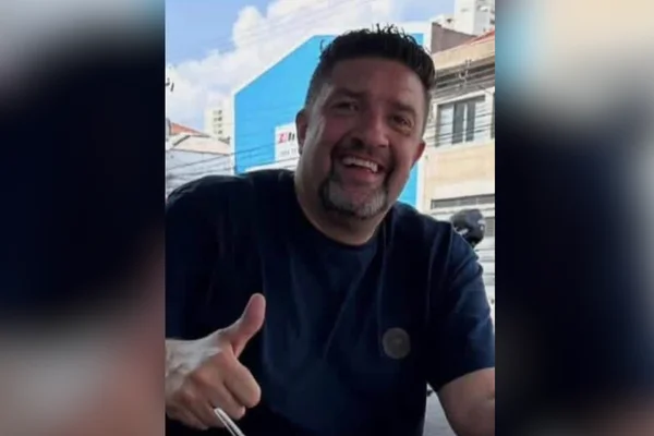 Imagem colorida de homem sorrindo e fazendo gesto de joia com a mão. Metrópoles