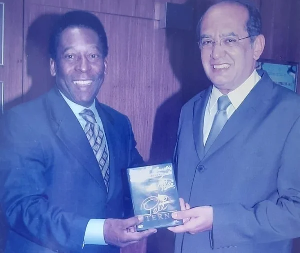 O ex-jogador Pelé entrega DVD com sua cine-biografia ao ministro do STF Gilmar Mendes, e ambos sorriem - Metrópoles