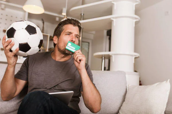 foto colorida de homem segurando bola de futebol sentado em um sofá branco