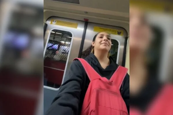 Imagem colorida mostra mulher jovem, pele morena, com o cabelo comprido cacheado castanho escuro preso em uma porta do Metrô de São Paulo - Metrópoles