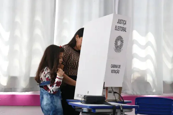 Foto colorida de eleitora votando acompanhada da filha na Escola Municipal de Ensino Fundamental - Metrópoles