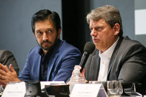O prefeito de São Paulo, Ricardo Nunes, observa o governador de São Paulo, Tarcísio de Freitas, durante discurso em cerimônia oficial