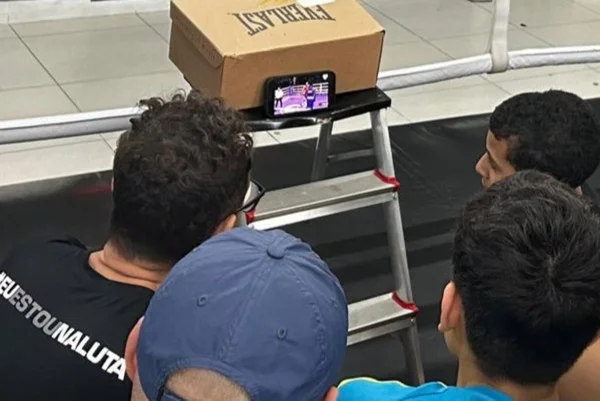 Imagem colorida mostra pessoas assistindo imagens de uma luta de boxe no celular - Metrópoles