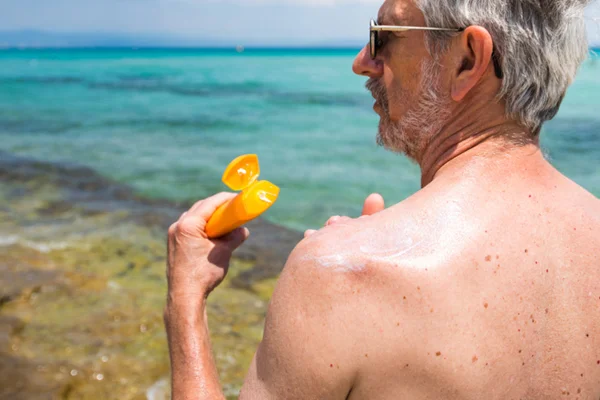 Homem grisalho passa protetor solar na praia - Metrópoles