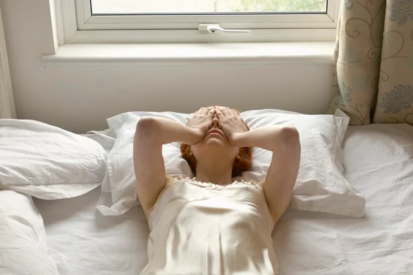 Na foto, uma mulher deitada na cama com crise de ansiedade