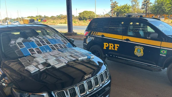 celulares em cima de um carro e, ao lado, uma viatura da prf