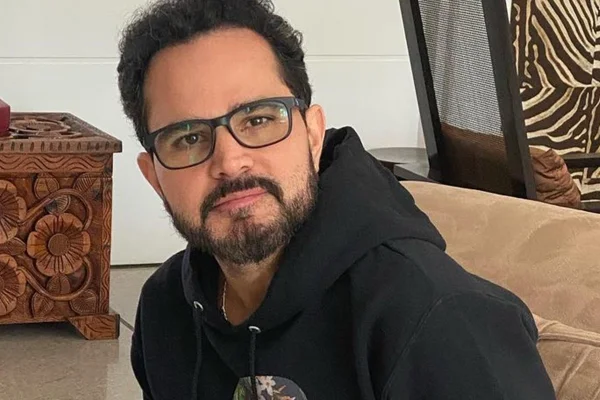 Luciano Camargo posa de casaco preto e óculos - Metrópoles