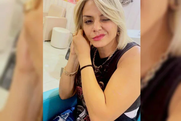 Mulher loira com blusinha preta, batom rosa ajusta brinco - Metrópoles