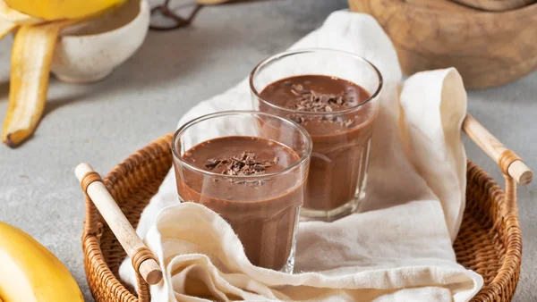 Foto colorida de milk shake de cacau com bananas ao lado
