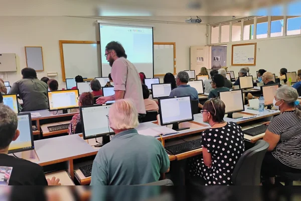 Imagem colorida de uma sala de aula com diversos alunos frente a um computador