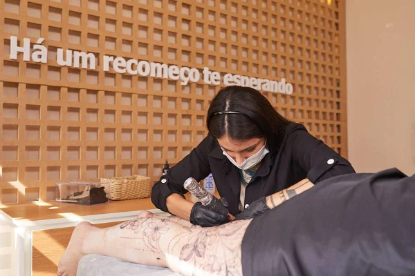 foto colorida de tatuadora fazendo tatuagem em perna de mulher - metrópoles