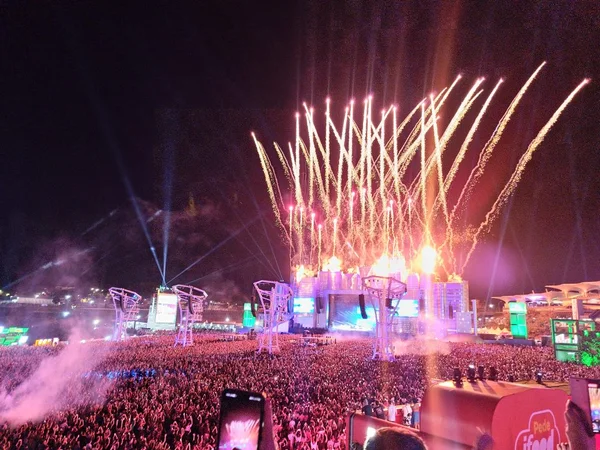 Imagem noturna e colorida mostra multidão em frente a palco de festival de música - Metrópoles