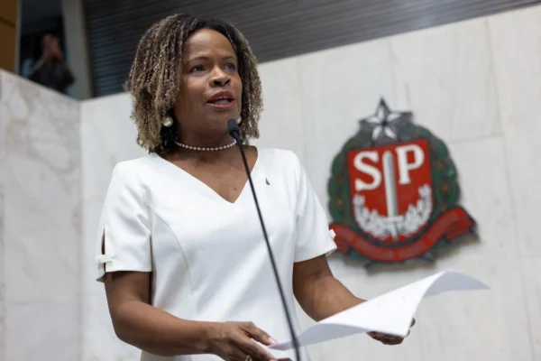 imagem colorida mostra coronel helena reis em discurso na assembleia legislativa de sp. ela é uma mulher negra, tem os cabelos na altura dos ombros, e veste uma blusa branca. nas mãos ela segura uma folha de papel
