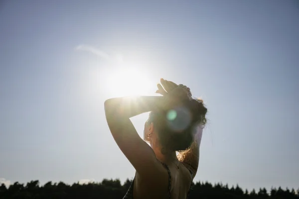 Imagem mostra mulher com os braços para cima recebendo a luz do sol - Metrópoles